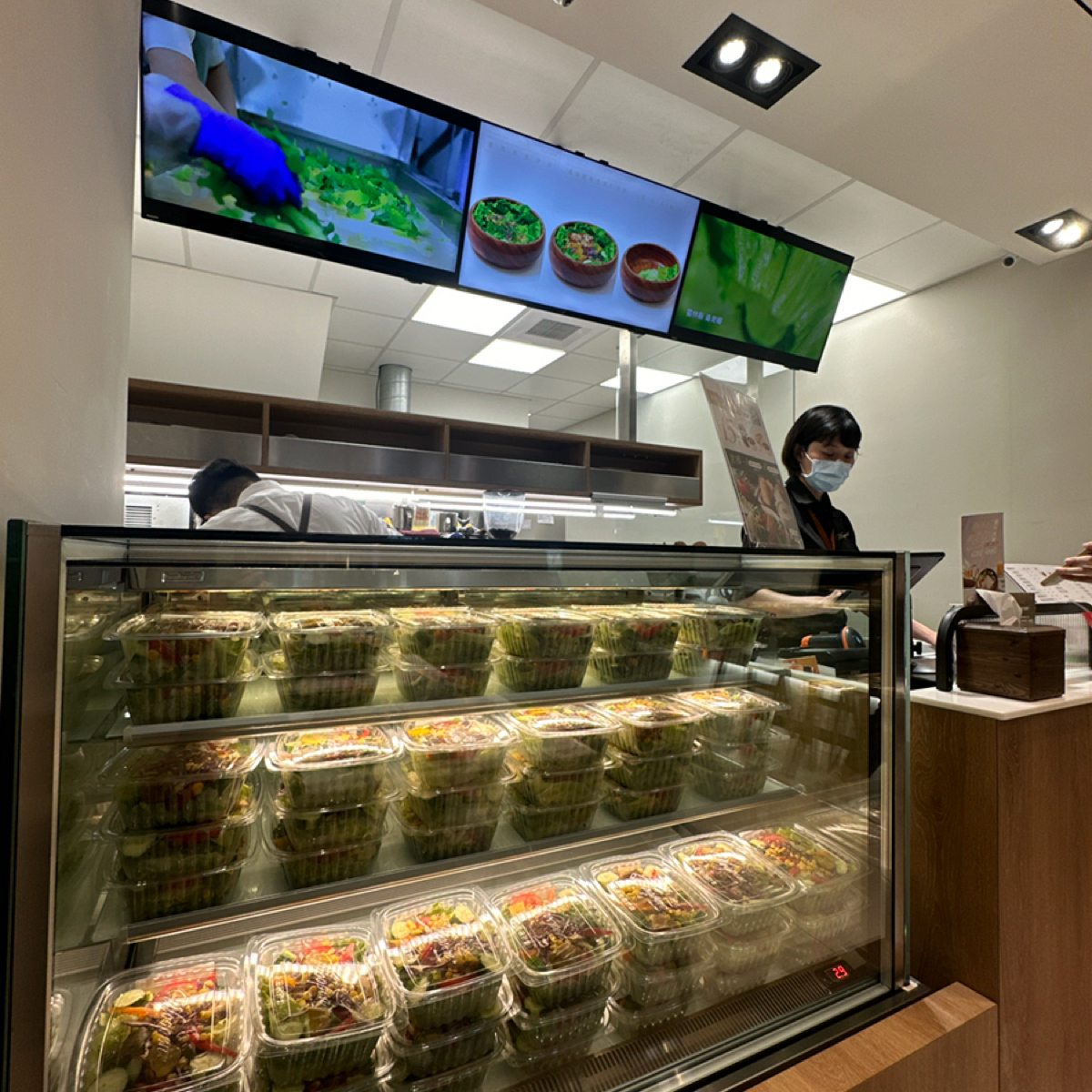 Vibe image of Woopen 木盆 永春門市: 店內的櫃檯，前面的展示冷藏櫃裡面有很多現成的沙拉餐盒，外帶的話很方便。後面廚房也可以看到他們在盛裝沙 shot by 阿波卡